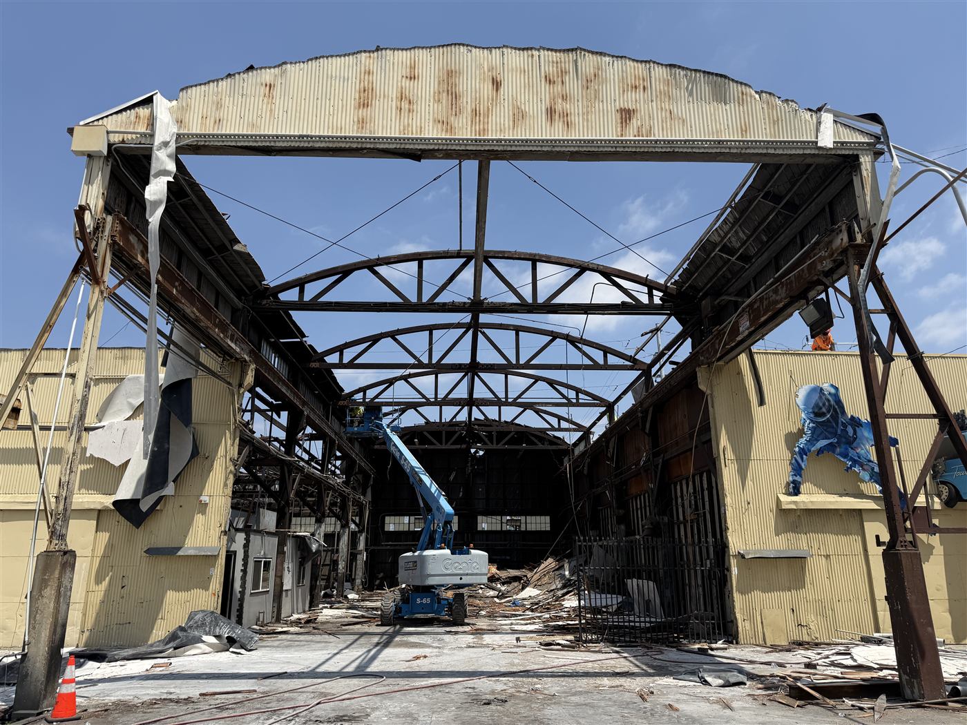 Excavator demolishing a tan commercial building near a parking structure