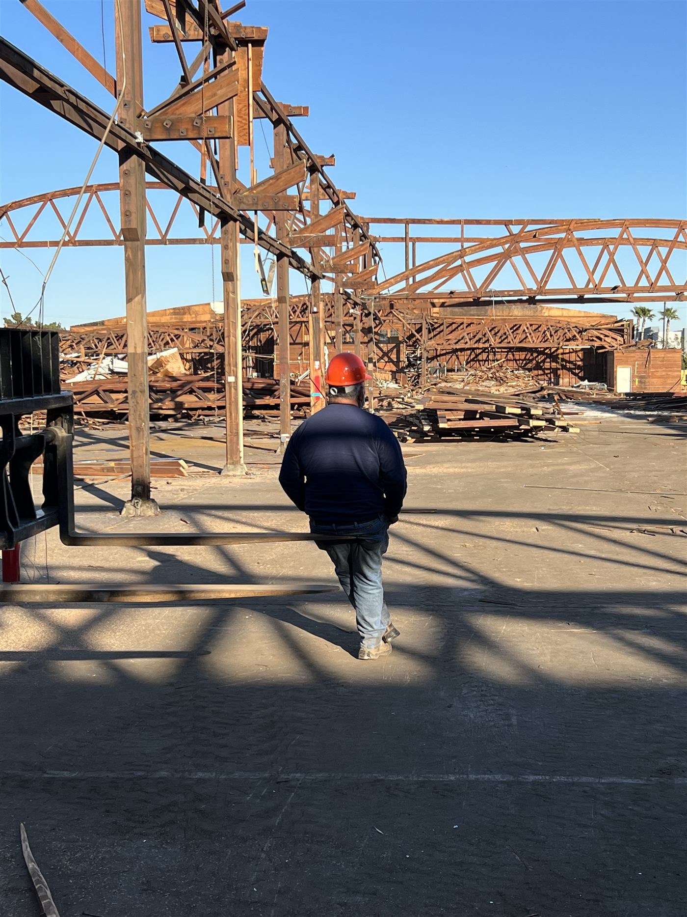 Worker in a hard hat surveying a demolished wood truss building at sunset
