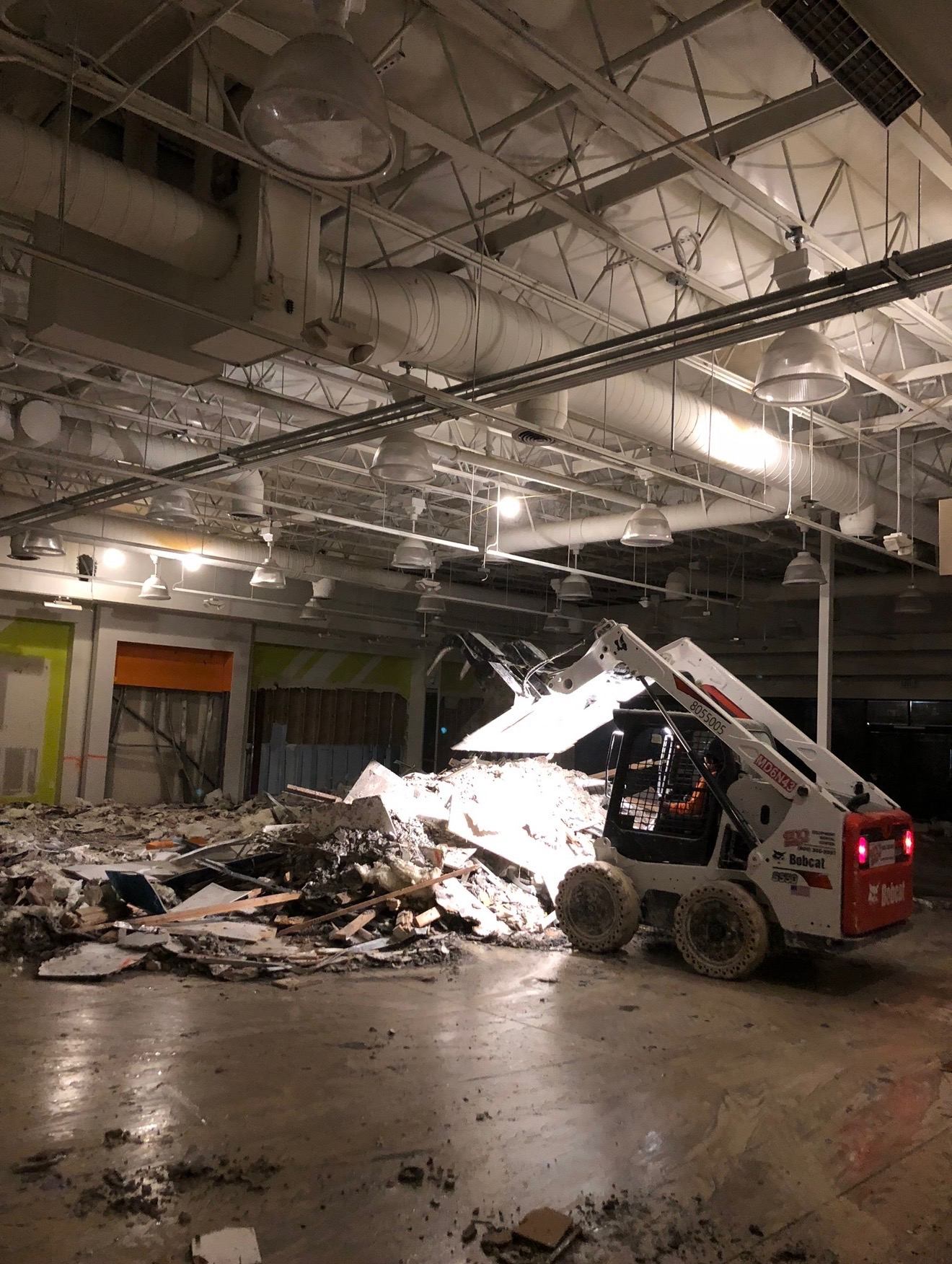 Skid-steer clearing interior demolition debris inside a commercial space